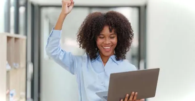 Mujer mirando felizmente su computadora portátil después de aprender a ocultar filas en Excel según el valor de la celda