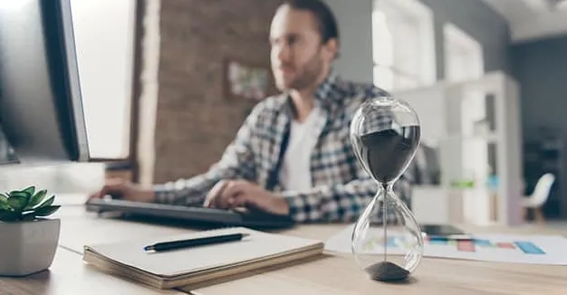 Hombre sentado frente a una computadora con un reloj de arena tratando de aprender cómo mejorar en Excel