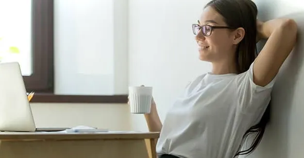 Mujer sentada frente a una computadora portátil con una taza de café mientras aprende las mejores habilidades de Excel